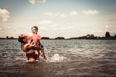 Playful mother and son having fun in water during summer day.