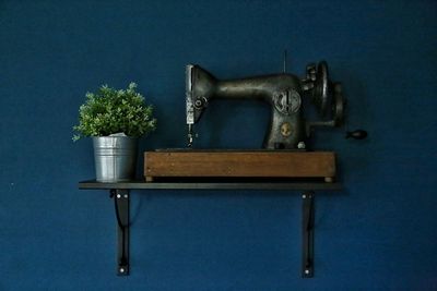 Old sewing machine by potted plant over shelf mounted on blue wall