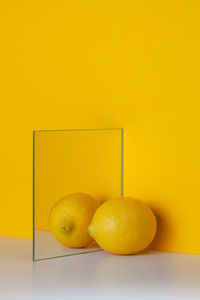 Yellow lemon is reflected in a mirror on a yellow background