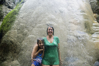 Happy woman with daughter standing by rocks at bua thong waterfalls