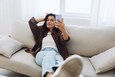 Young woman using mobile phone while sitting on sofa at home