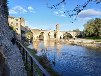 Arch bridge over river by building against sky