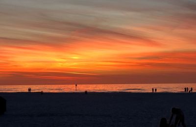 Silhouette people on beach against orange sky