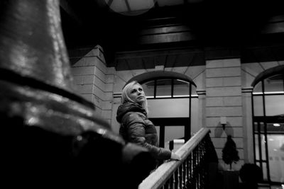 Woman standing by railing against house at night