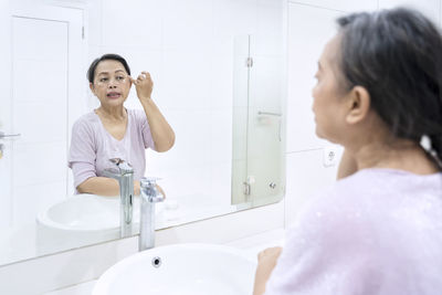 Senior woman looking in mirror at bathroom