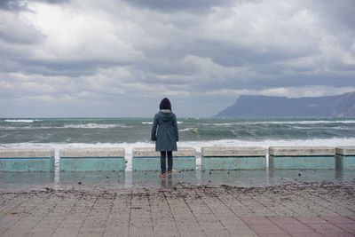 Rear view of man standing on beach against cloudy sky