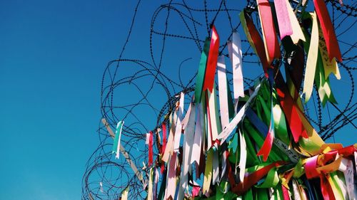 Low angle view of ribbons on barbed wire against clear blue sky during sunny day