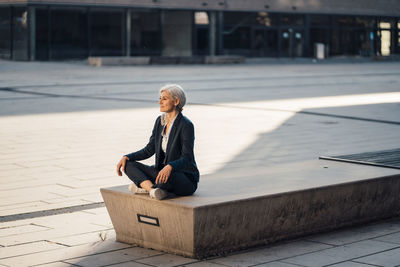 Businesswoman sitting with cross-legged on bench at office park