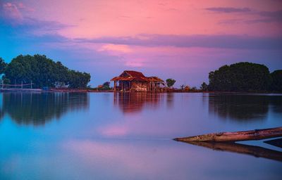 Scenic view of lake by building against sky during sunset