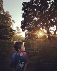Boy looking away while standing on land against sky during sunset