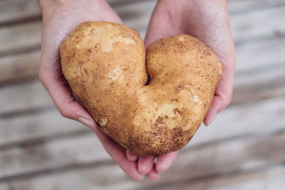 Cropped hands of woman holding heart shape raw potato over table