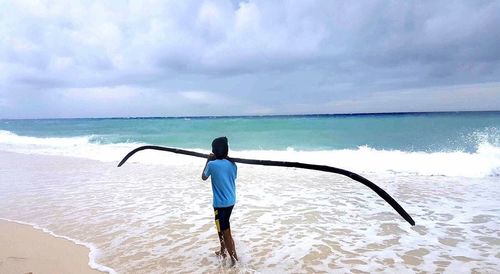 Rear view of man standing at beach against sky