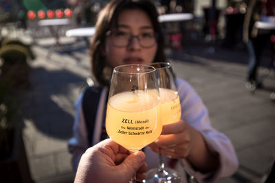 Cropped hand toasting drink with woman outdoors