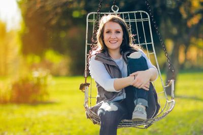 Portrait of smiling woman sitting on swing at backyard