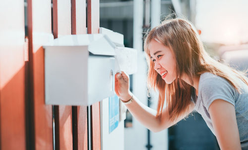 Side view of smiling young woman looking in mailbox
