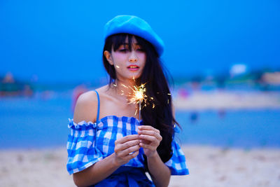 Young woman standing at beach against blue sky