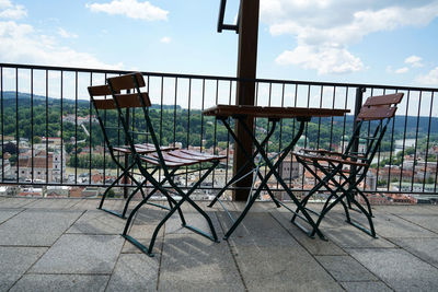 Empty chairs and tables in balcony against sky