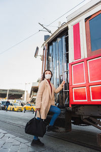 Full length of woman wearing mask standing by tramway against sky