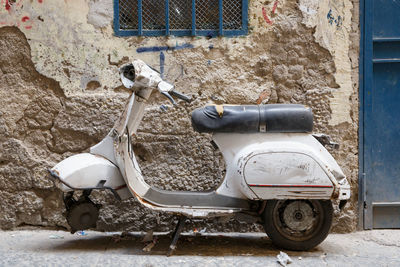 Abandoned motor scooter parked by weathered wall on street