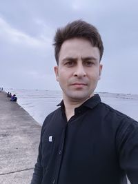 Portrait of young man standing by sea against sky