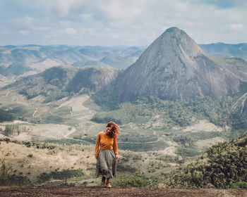 Rear view of man standing on mountain against sky