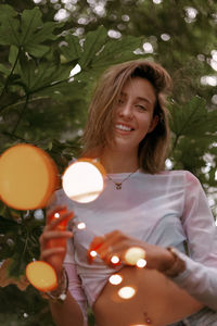 Portrait of smiling young woman standing against trees