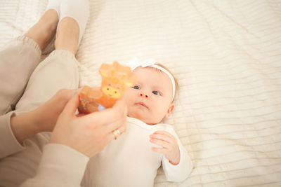 Child lies on bed, plays with toy, mother teaches her daughter, newborn baby in bedroom. 