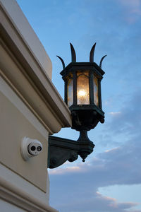 Low angle view of illuminated street light on wall against cloudy sky