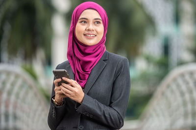 Portrait of a smiling young woman using smart phone outdoors
