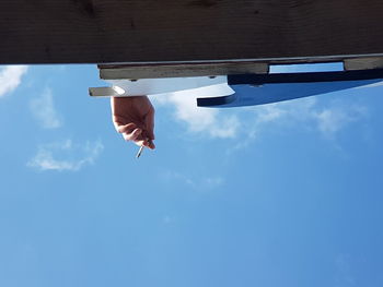 Low angle view of cropped hand holding cigarette against sky