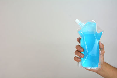 Close-up of hand holding drink against blue background