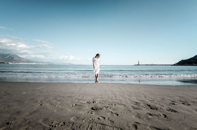 Full length of woman standing on shore at beach against sky