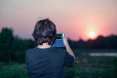 Rear view of man photographing sky during sunset