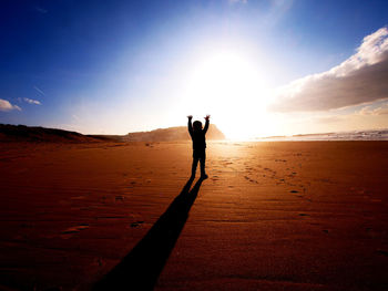 Silhouette child standing at beach against sky during sunset