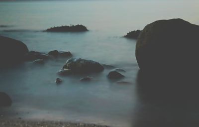 Rocks in sea against sky at sunset