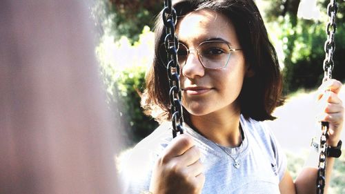 Close-up portrait of girl holding chain while sitting on swing