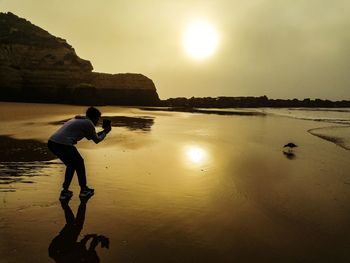 Side view of man on beach against sky during sunset