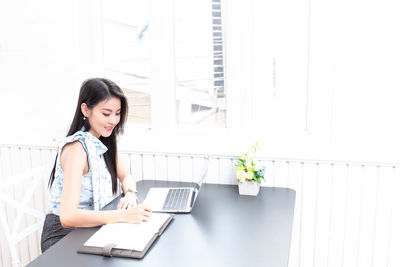 Young woman using phone while sitting on table