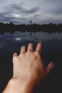Close-up of hand gesturing against lake