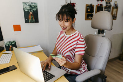 Young woman with credit card shopping online through laptop at home