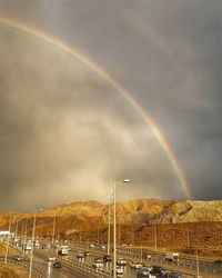 Rainbow over road against cloudy sky