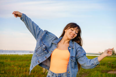 Happy young woman standing on field against sky