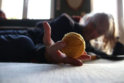 Surface view of woman holding ball of wool lying on floor at home