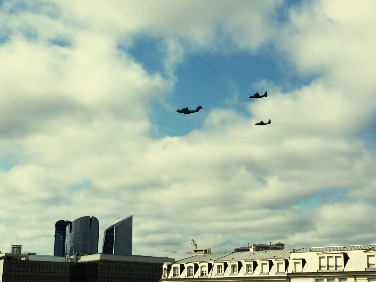 low angle view, sky, flying, cloud - sky, architecture, building exterior, built structure, airplane, cloudy, air vehicle, transportation, cloud, bird, city, mid-air, mode of transport, outdoors, day, travel, overcast