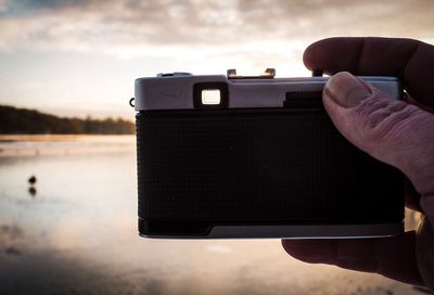 Cropped hand of man holding camera against sky