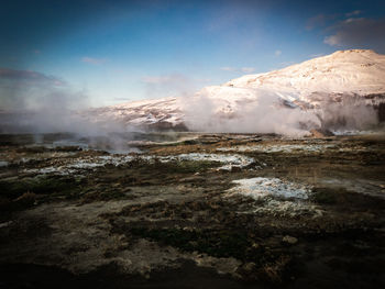 Scenic view of hot springs with snowcapped mountains against sky