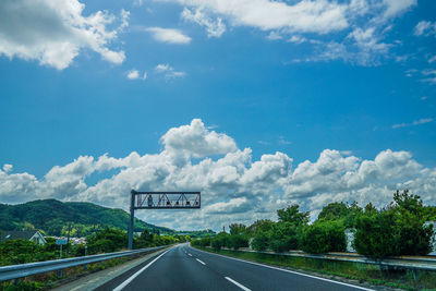 Road sign by trees against sky