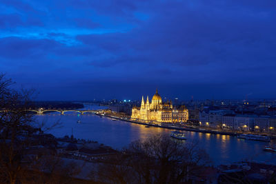 Illuminated city at waterfront against cloudy sky