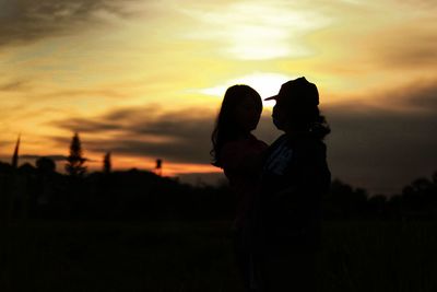 Silhouette couple standing on field against sky during sunset