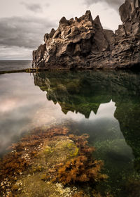 Rock formation by lake against sky